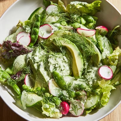Fresh Green Salad with Green Goddess Dressing on a plate, garnished with radishes and snap peas.