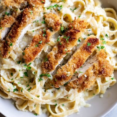 Golden crispy chicken Alfredo topped over creamy fettuccine pasta on a rustic plate