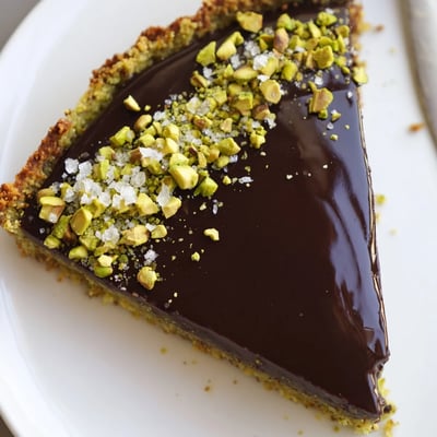 Silky dark chocolate pistachio tart sliced and plated on a rustic ceramic dish