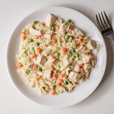 A steaming bowl of Creamy Chicken Pot Pie Orzo topped with fresh parsley and parmesan.
